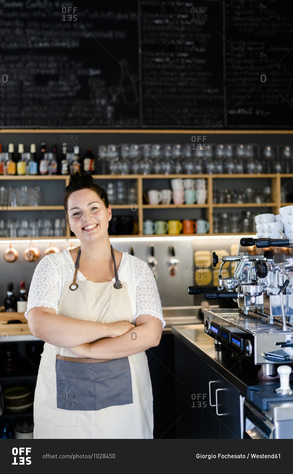 Smiling female entrepreneur with arms crossed standing in cafe