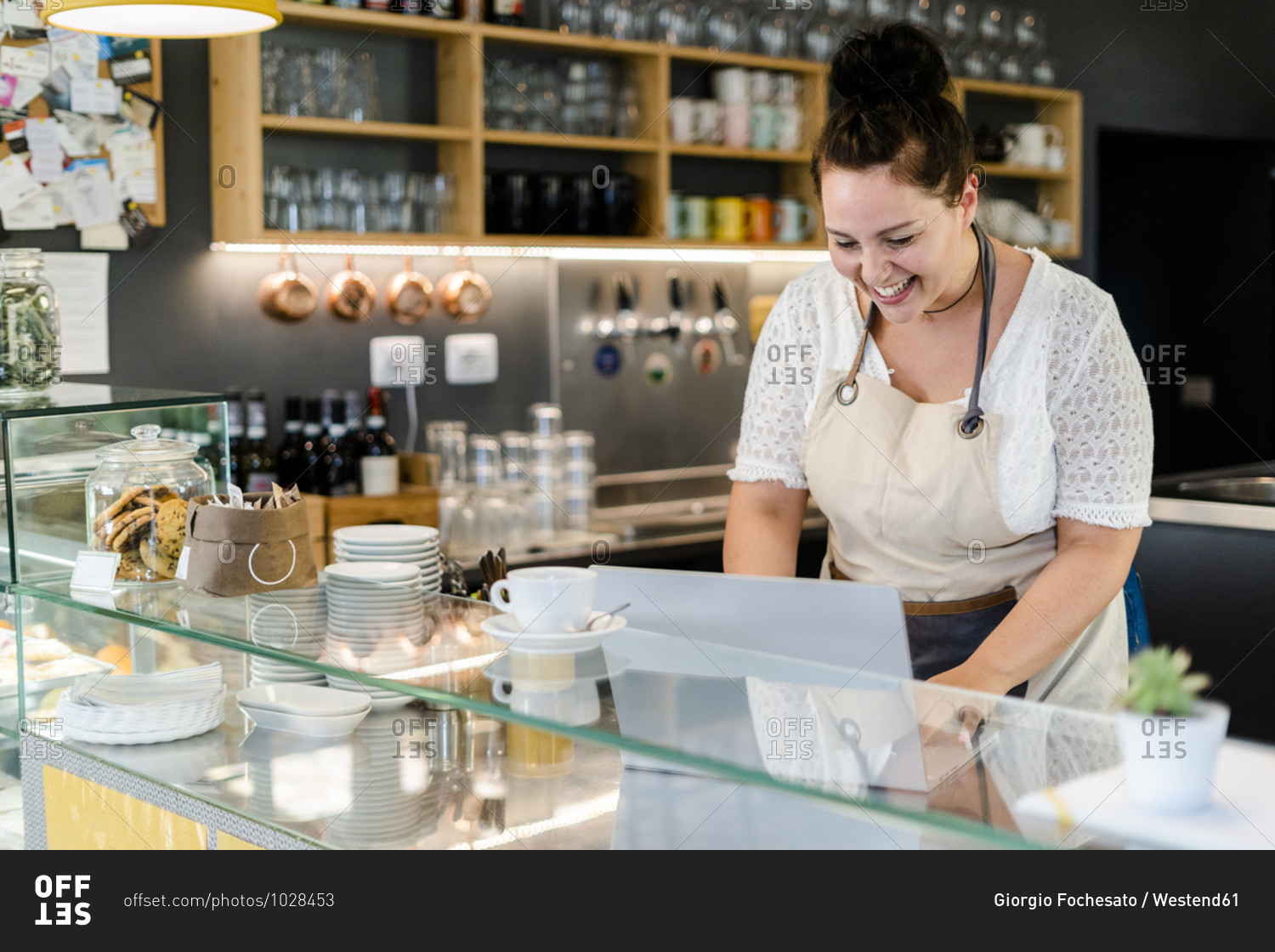 Cheerful female owner using laptop while standing in coffee shop