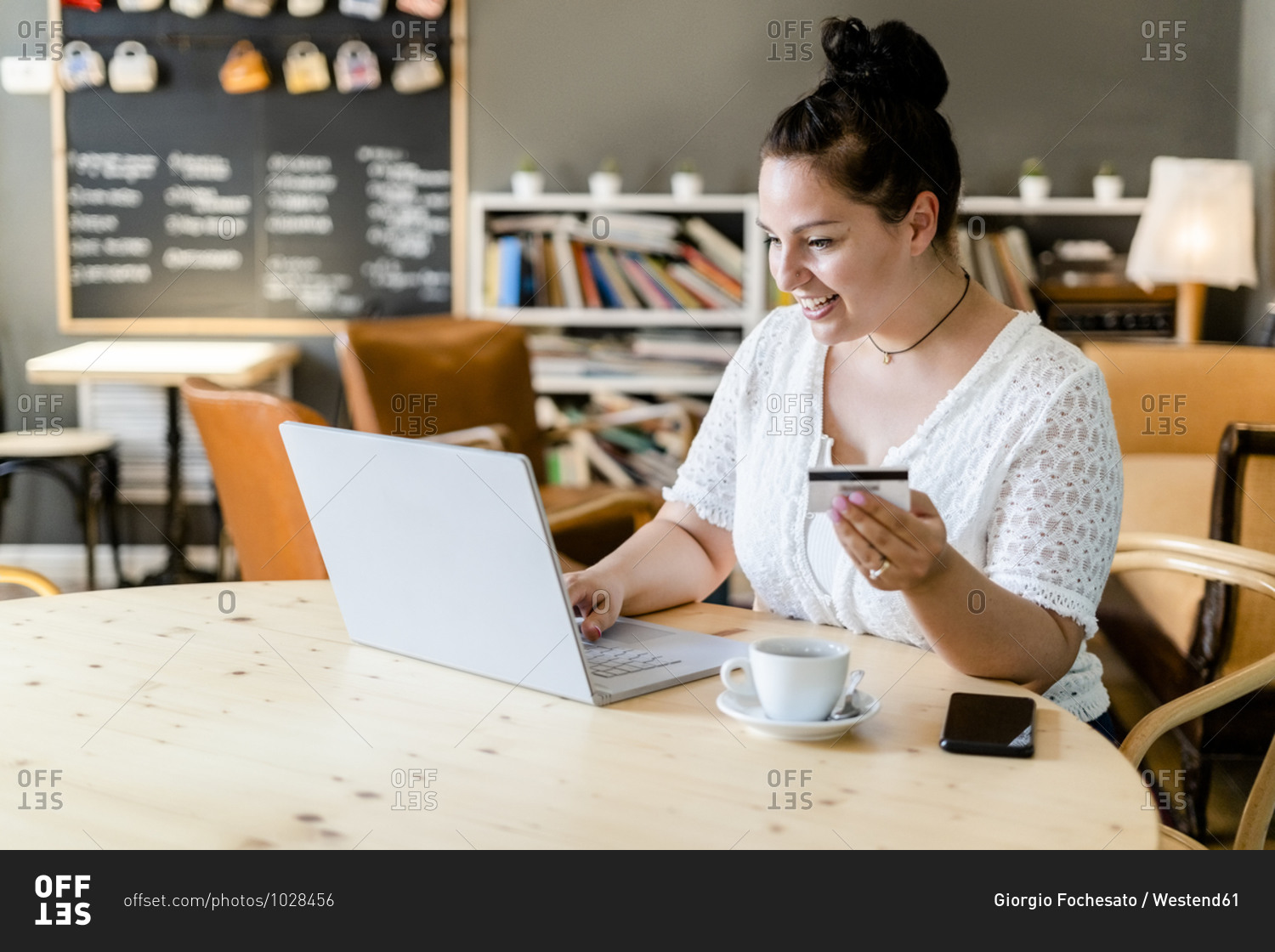 Happy young woman doing online shopping over laptop in coffee shop