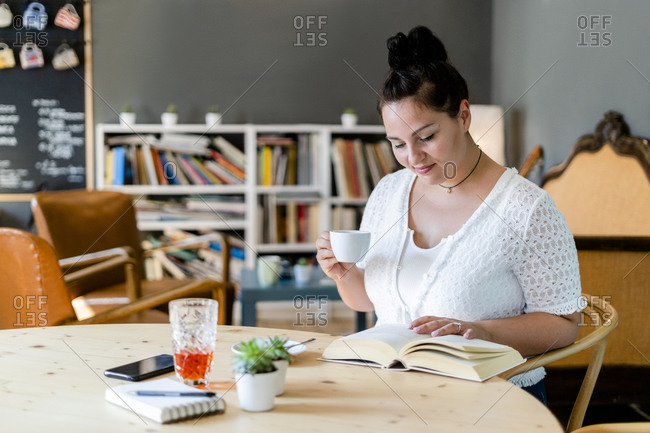 Voluptuous woman holding coffee cup while reading book on table in restaurant