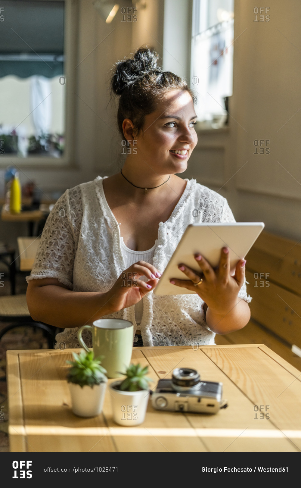 Smiling voluptuous woman using digital tablet looking away while sitting at table in cafe