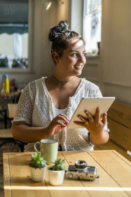 Smiling voluptuous woman using digital tablet looking away while sitting at table in cafe