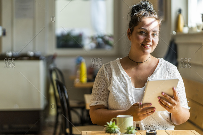 Smiling voluptuous woman using digital tablet while sitting in coffee shop