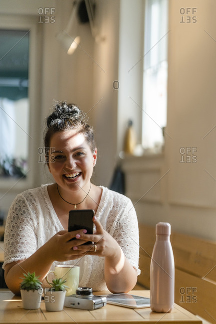 Cheerful voluptuous woman using mobile phone while sitting at table in coffee shop