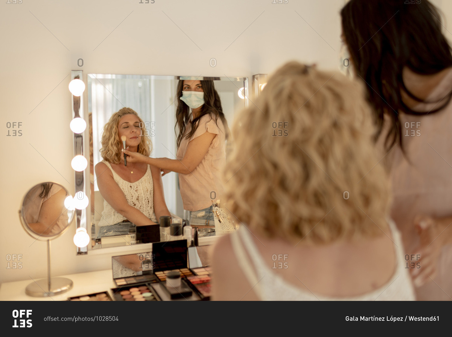 Make-up artist wearing mask applying blusher to customer while looking in mirror at studio