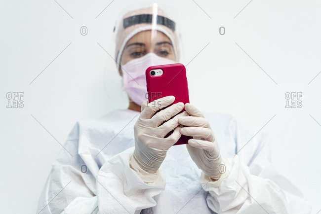 Dentist in protective workwear using mobile phone at office