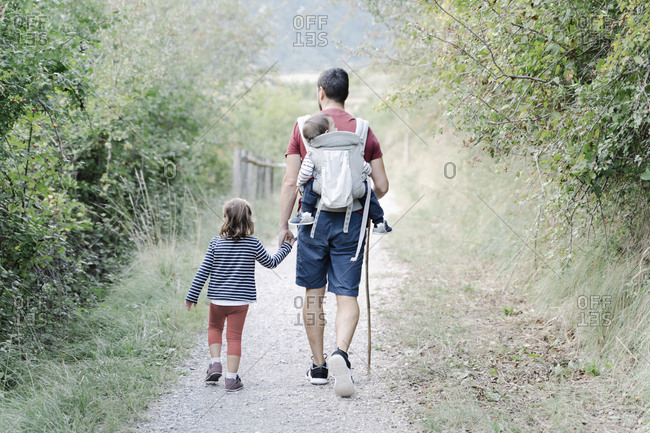 Father hiking with his children- carrying son on back while holding hand of daughter