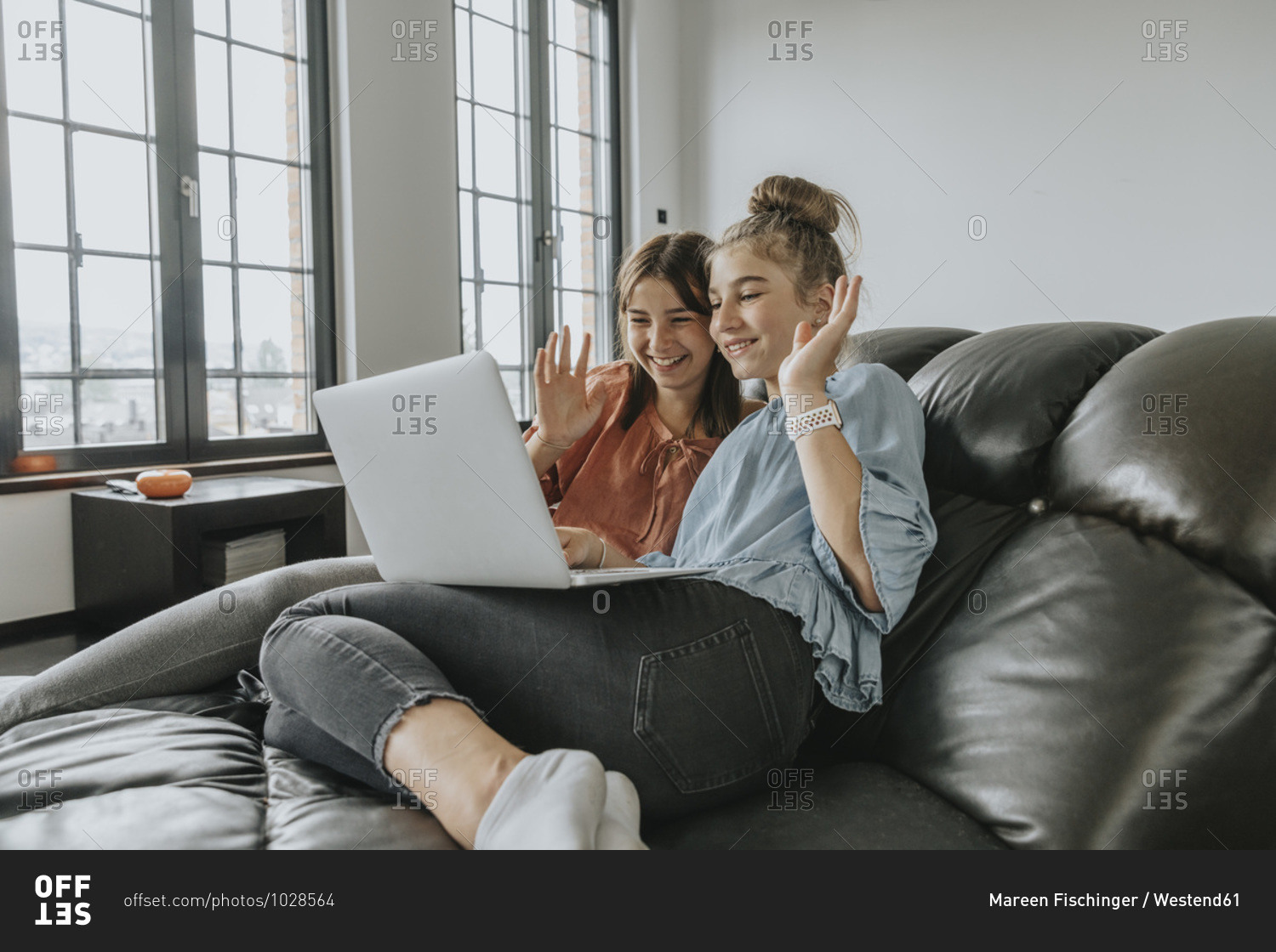 Friends waving while video conferencing over laptop on sofa at home