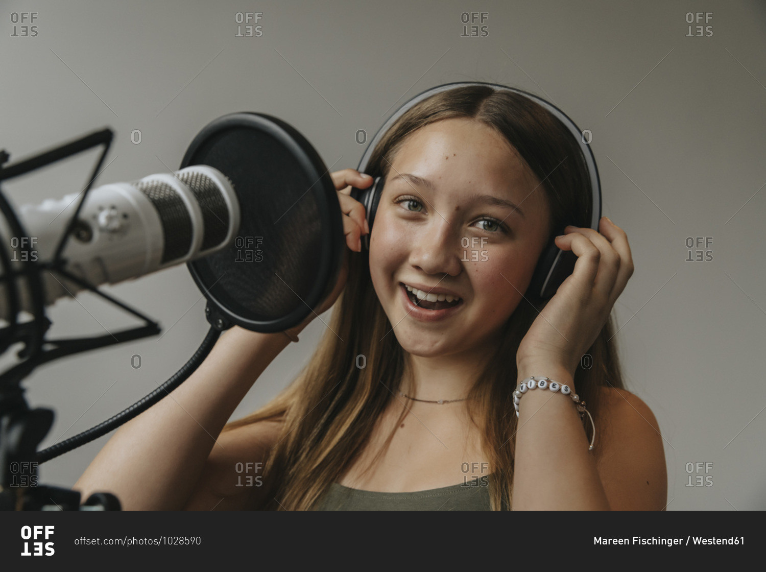 Close-up portrait of happy teenage girl singing against wall in recording studio