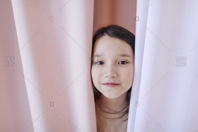 Girl hiding behind curtain at home