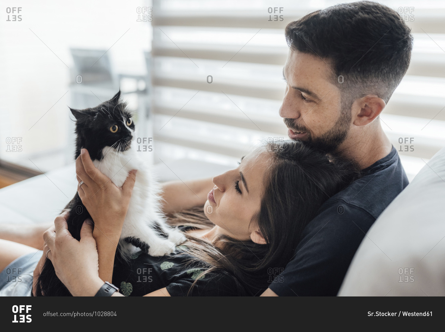 Couple sharing tenderness with cat while sitting at home