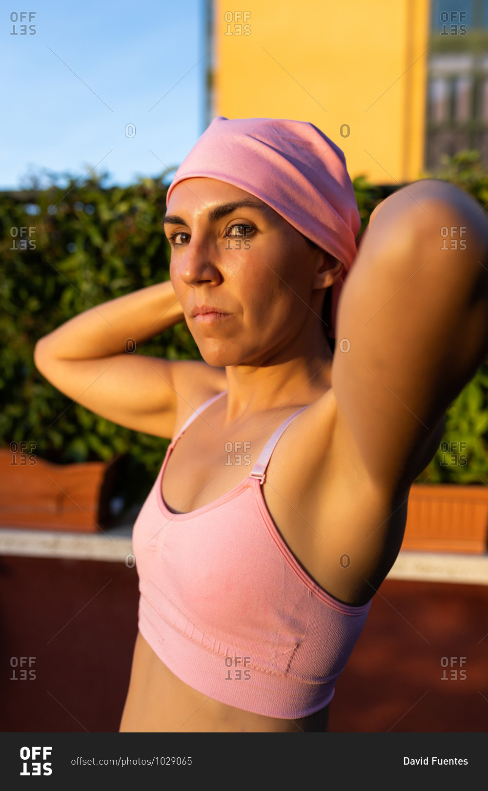 Young brunette woman stretching after training wearing the pink headscarf, symbol of a woman\'s fight against breast cancer.