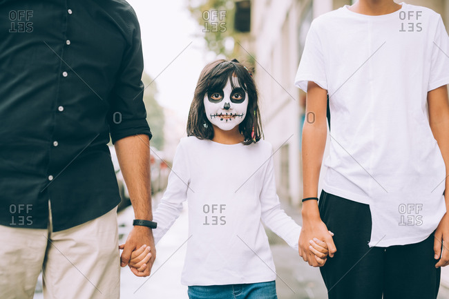 Girl with Halloween face paint, holding parents' hands
