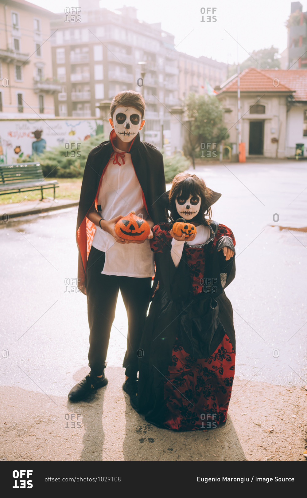 Brother and sister in Halloween costumes holding painted pumpkins stock