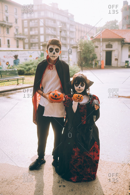 Brother and sister in Halloween costumes holding painted pumpkins
