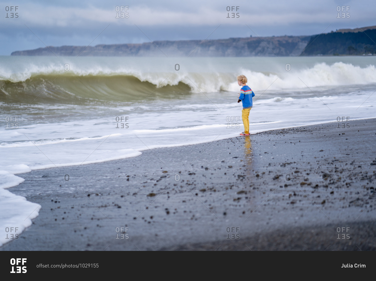 Little boy watching fierce waves roll into the beach shore