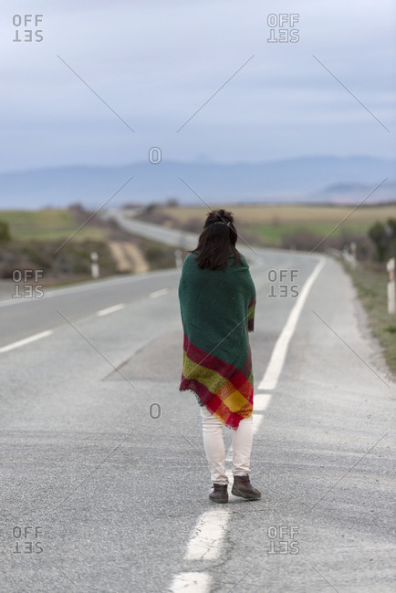 Woman walking down a road, wrapped in a blanket