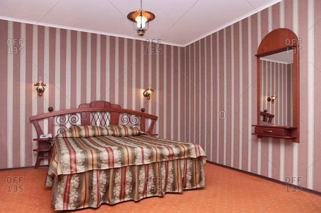 Estonia - September 22, 2020: A hotel with old fashioned retro styled rooms, a bedroom with checked bedding, striped wallpaper and mirror.