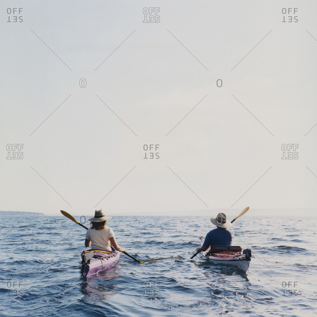 Middle aged man and woman sea kayaking at dusk