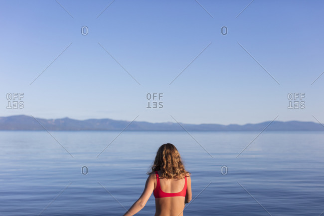 View from behind of woman entering calm, blue waters of a lake at dawn