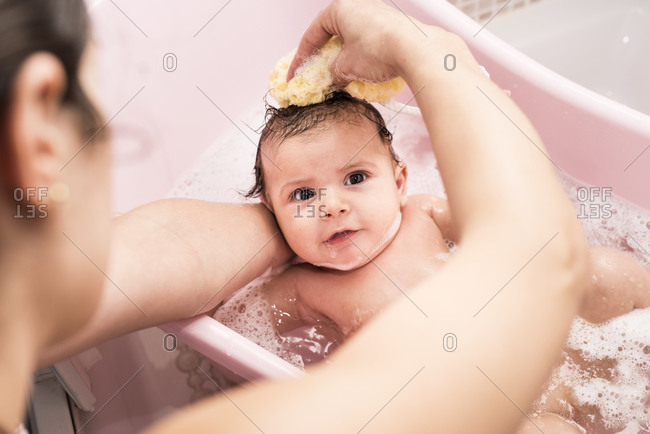 Mother cleaning 2 months baby in little bathtub. Little boy having a bath.