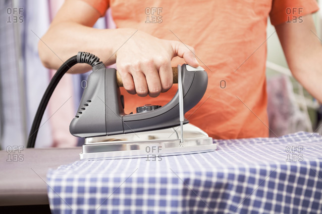 Close up of person wearing bright orange top ironing kitchen towels on ironing board and using modern iron appliance