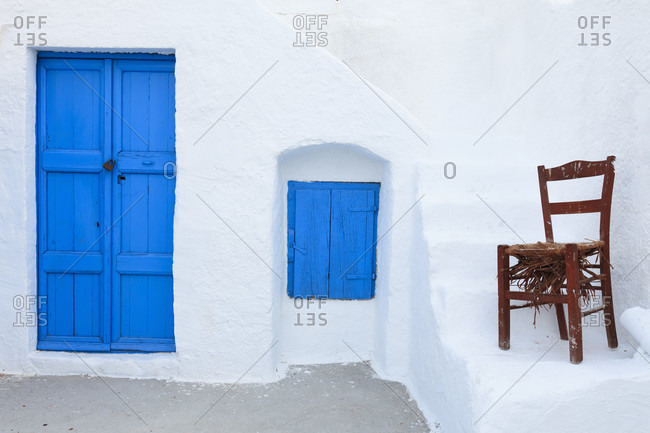 Blue painted closed door and window shutter by an old chair by white washed stairs