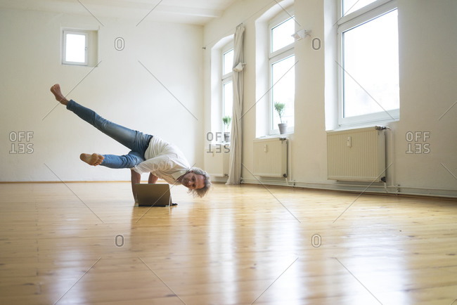 Mature man doing a handstand on floor in empty room looking at tablet