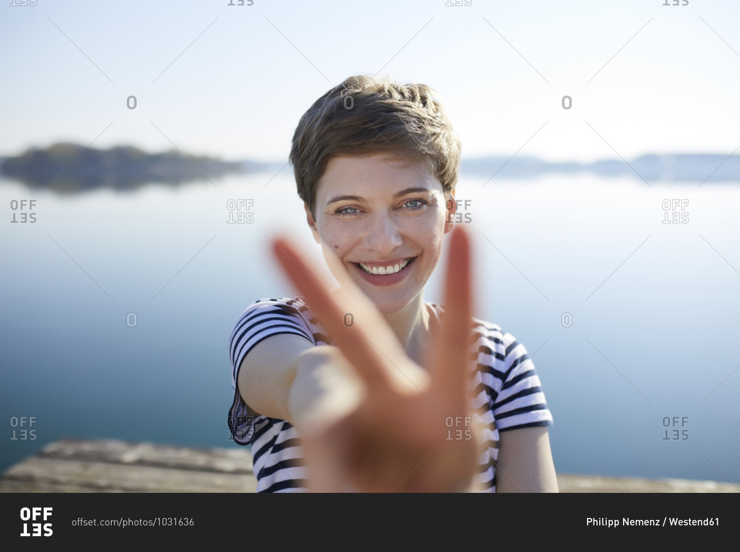 Portrait of smiling woman in front of lake showing victory sign