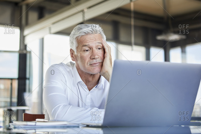Bored businessman sitting at desk- using laptop