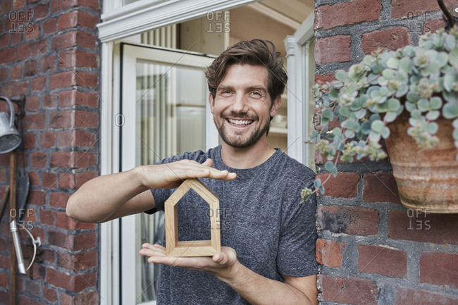 Portrait of smiling man at house entrance holding house model