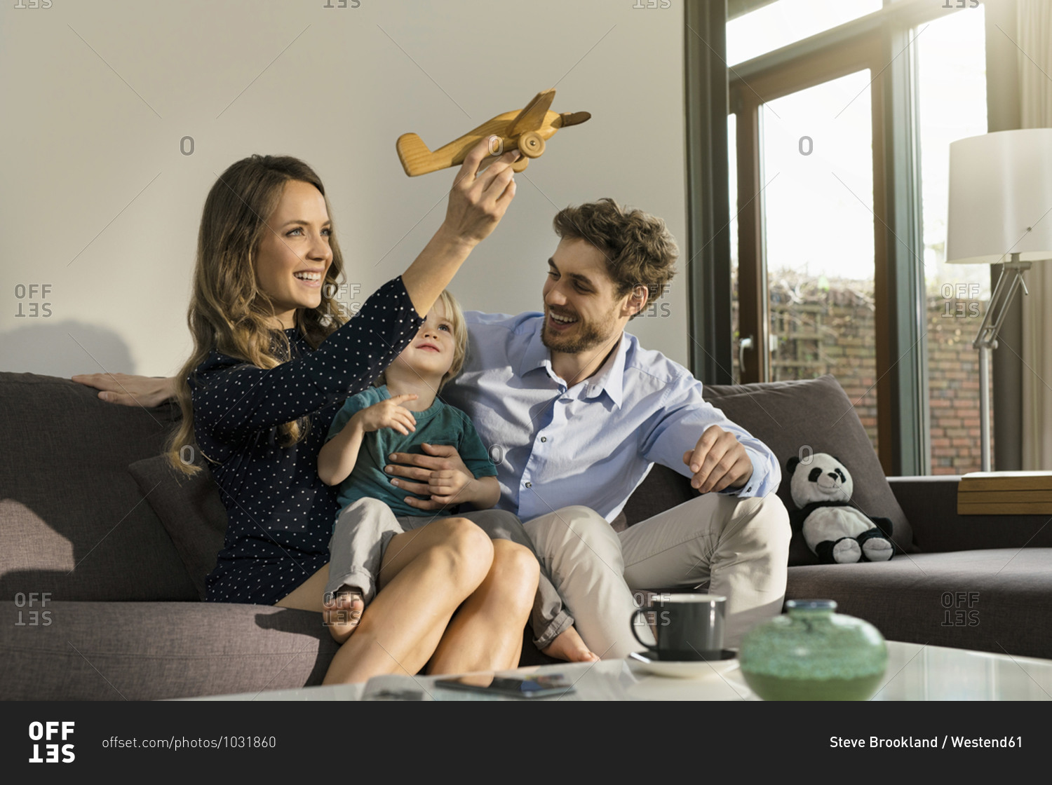 Happy parents and son playing with wooden toy plane on sofa at home