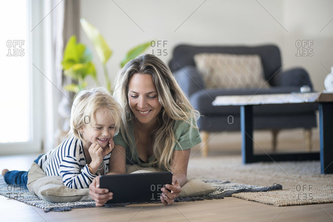 Smiling mother and son lying on the floor at home using tablet