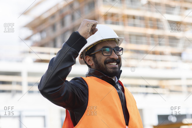 Portrait of happy construction engineer in front of construction site wearing hard hat and safety vest
