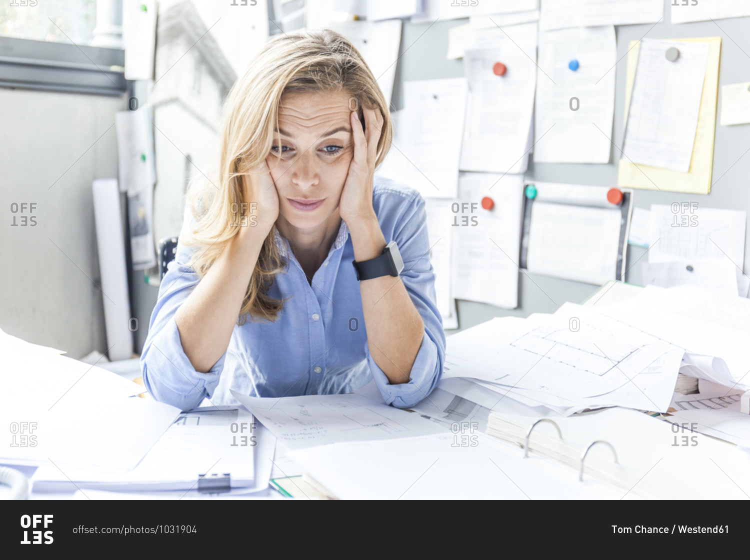 Stressed woman sitting at desk in office surrounded by paperwork