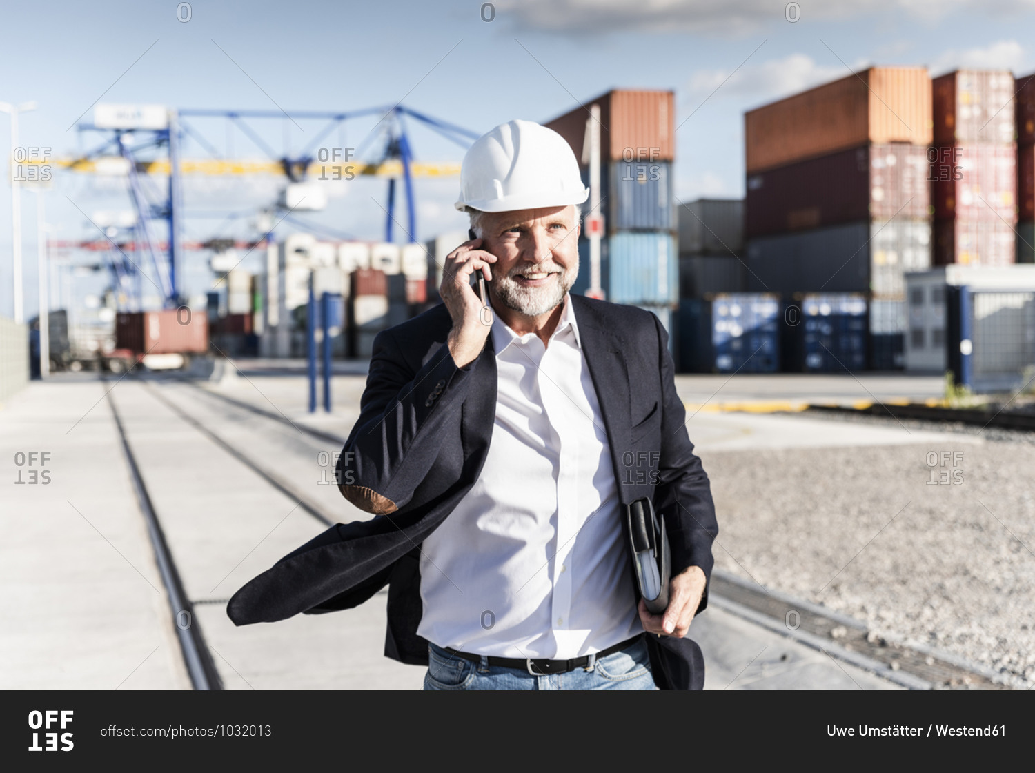 Businessman at cargo harbor- wearing safety helmet- using smartphone
