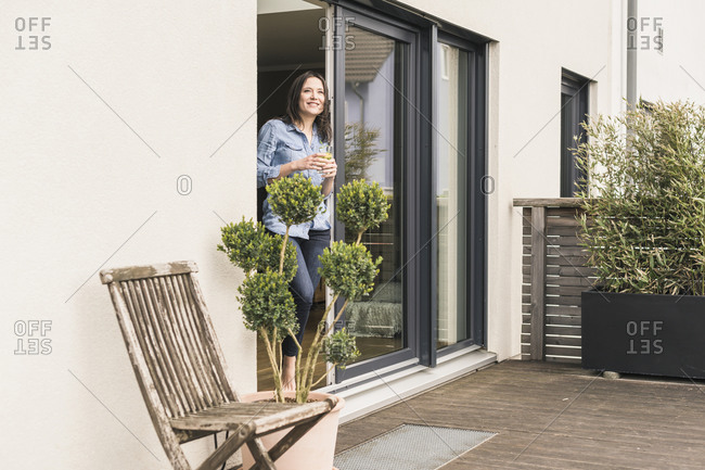Smiling woman standing at terrace door at home with healthy drink