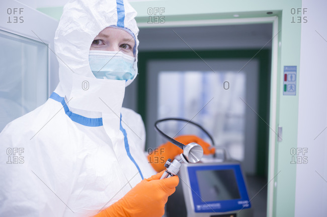 Lab technician wearing cleanroom overall holding apparatus at material sluice