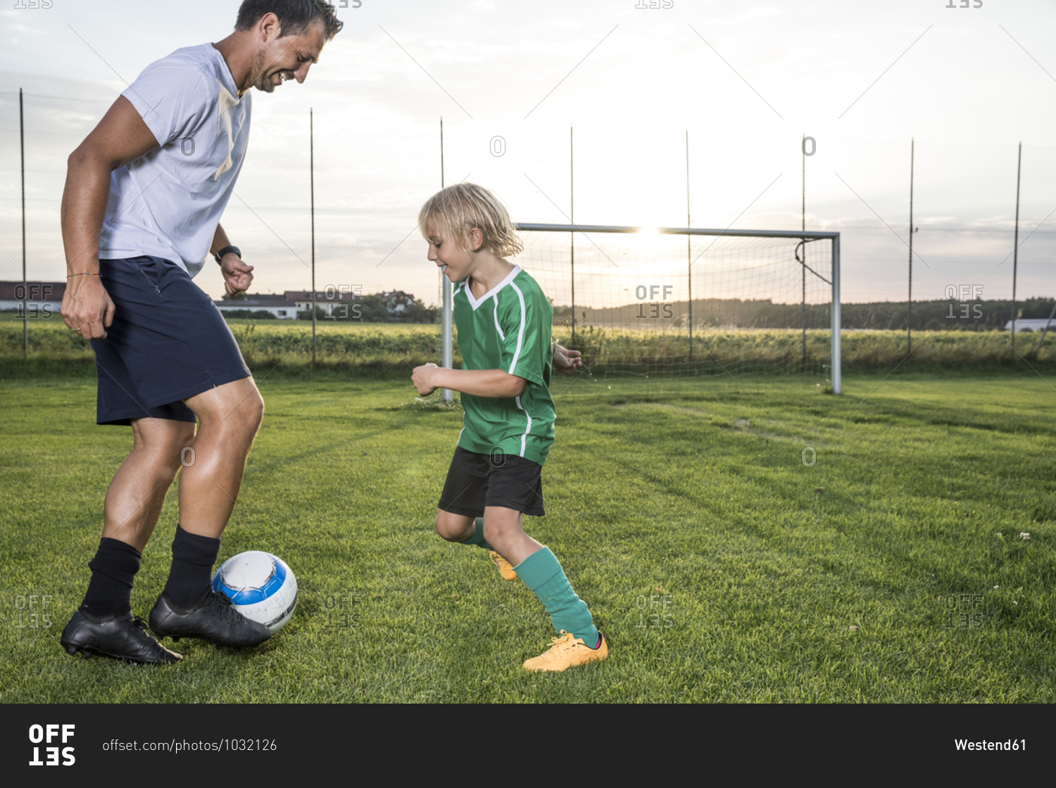 Coach and young football player on football ground at sunset