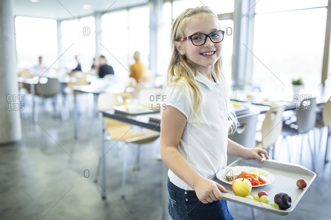 Portrait of smiling schoolgirl carrying tray in school canteen