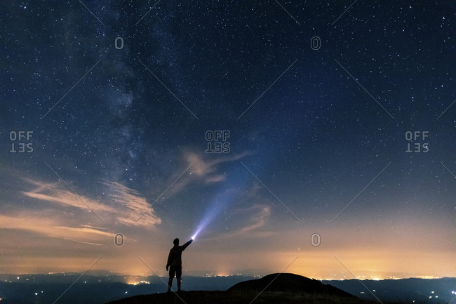 Italy- Monte Nerone- silhouette of a man with torch under night sky with stars and milky way