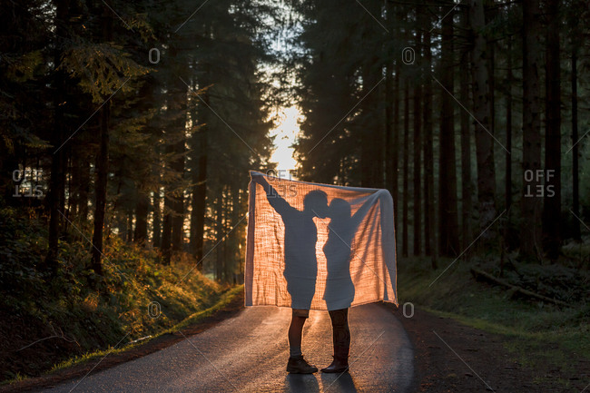 Silhouette of couple holding blanket kissing on country road in forest