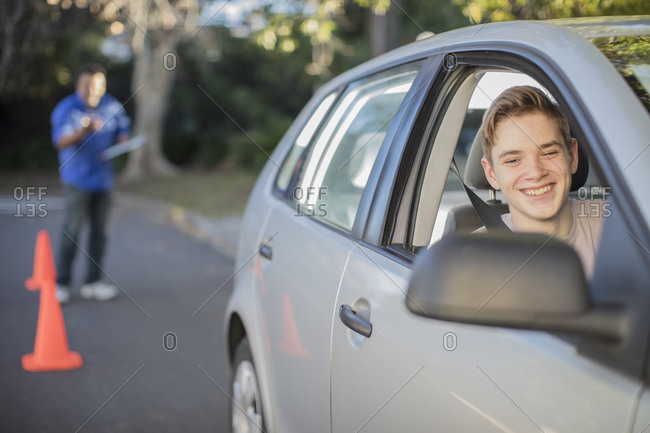 Smiling learner driver learning to drive looking at wing mirror of a car