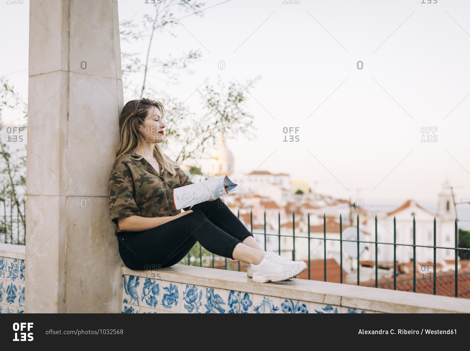 Young woman with map sitting on retaining wall against clear sky