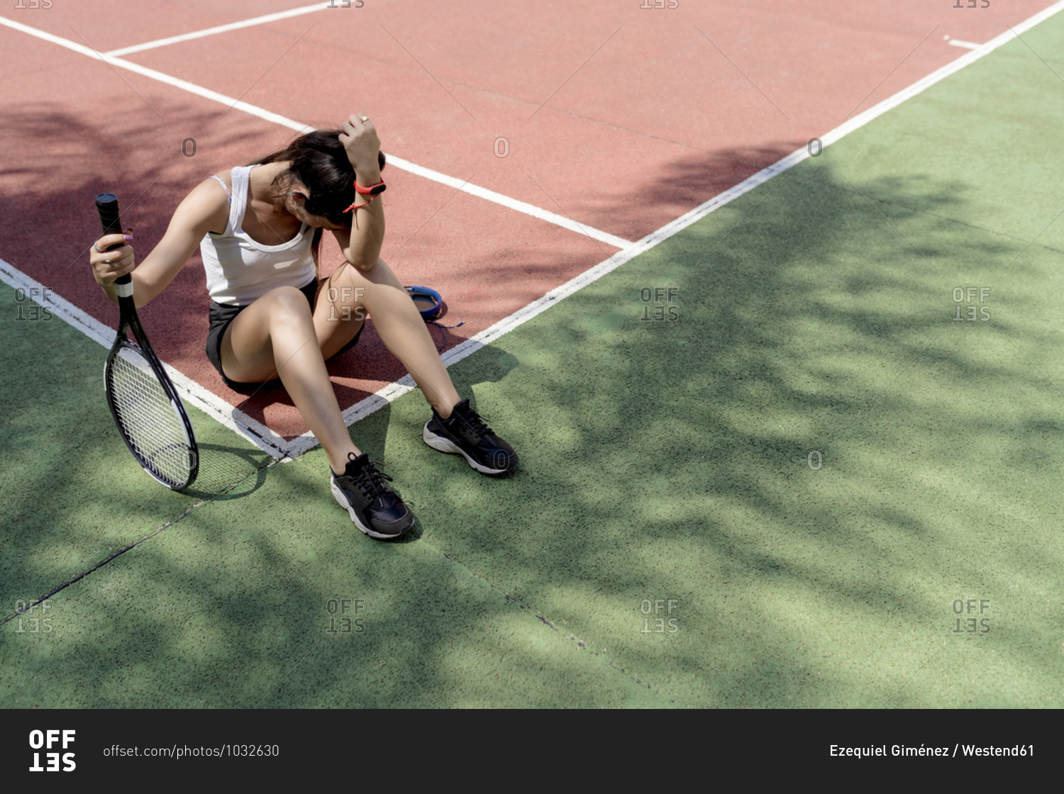 Sad female tennis player sitting on floor in sports court