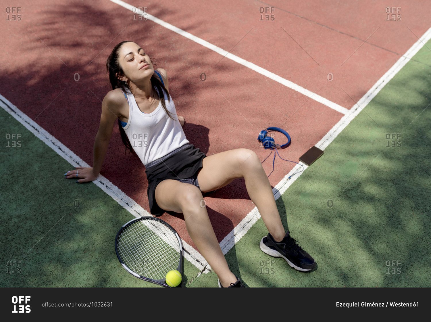 Female tennis player with eyes closed relaxing on floor in sports court