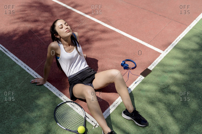 Female tennis player with eyes closed relaxing on floor in sports court