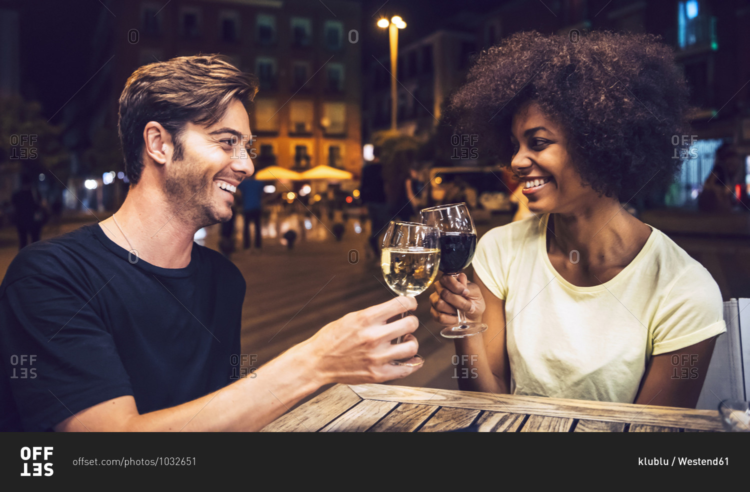 Cheerful couple looking at each other while toasting wineglasses at date night