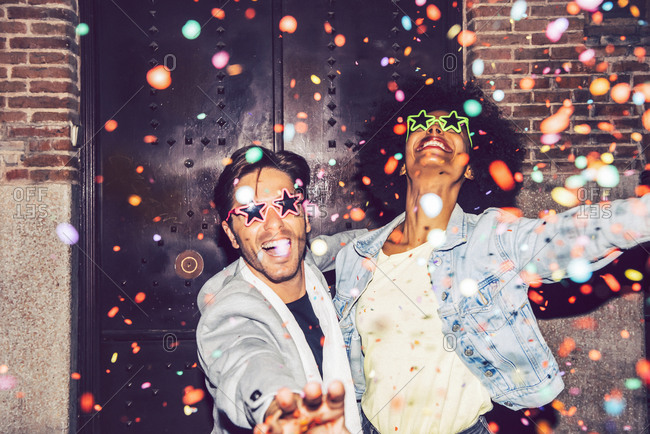 Confetti falling on cheerful couple wearing star shaped sunglasses enjoying outdoors at night