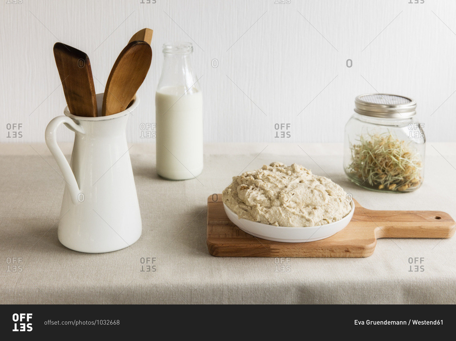 Jug with wooden spoon and spatula- milk bottle- jar of sprouts and dough on cutting board
